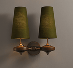 A Clérachic twin wall light with green shades, softly lit, on a grey wall above walnut discs and a bronze backplate.