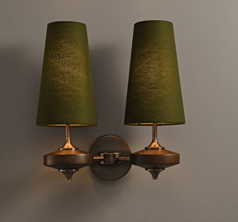 A Clérachic twin wall light with green shades, softly lit, on a grey wall above walnut discs and a bronze backplate.