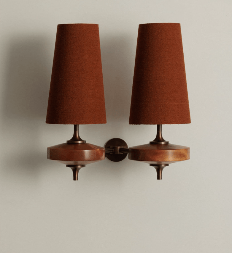 Two rust-brown shades on a Clérachic twin sconce, hung on a pale grey wall with walnut discs and a small round backplate.