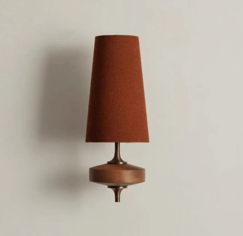 A single rust-brown shade over a walnut disc on this Clérachic wall sconce, against a light grey wall.