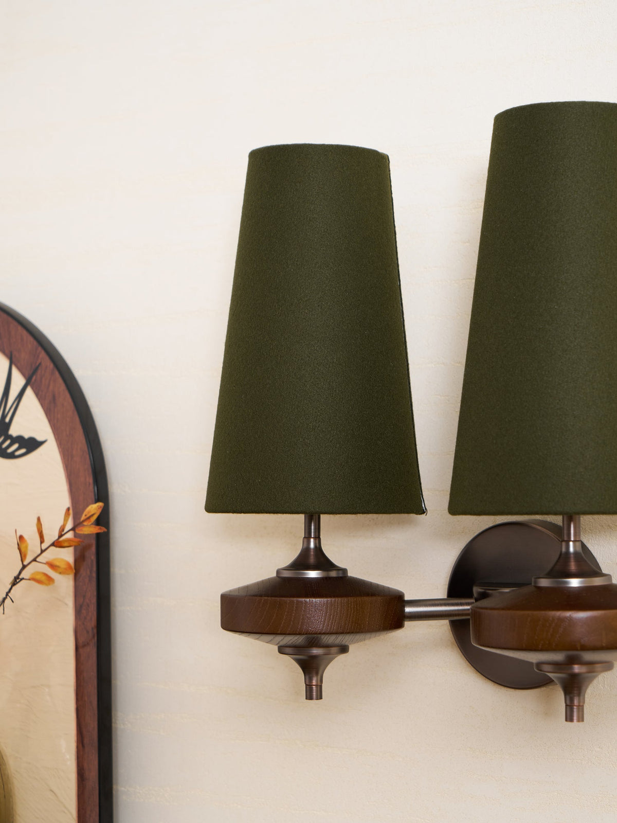 Cropped view of a Clérachic twin sconce with green shades beside an arched mirror on a cream wall.