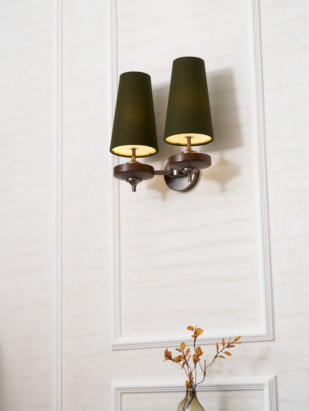 Warm light from the green shades of this Clérachic twin sconce, hung high on a white panelled wall above a bedside vase.