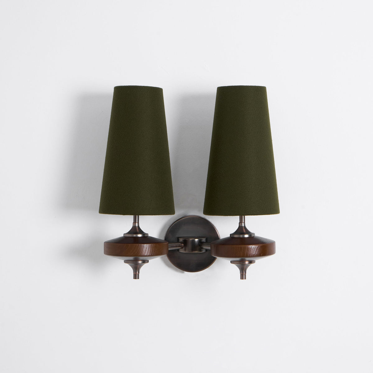 Green fabric shades, walnut discs and a bronze round backplate on a Clérachic twin wall sconce, on a light backdrop.
