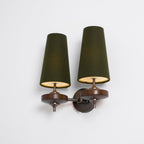 Lit green shades with a glowing gold underside on a Clérachic twin wall sconce, on a plain white background.