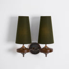 Softly lit green shades on a Clérachic twin wall light, with walnut discs and a bronze link arm on a plain white wall.