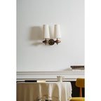 A Clérachic twin wall sconce with cream shades over a white mantel, a small jug and a round table with a linen cloth.