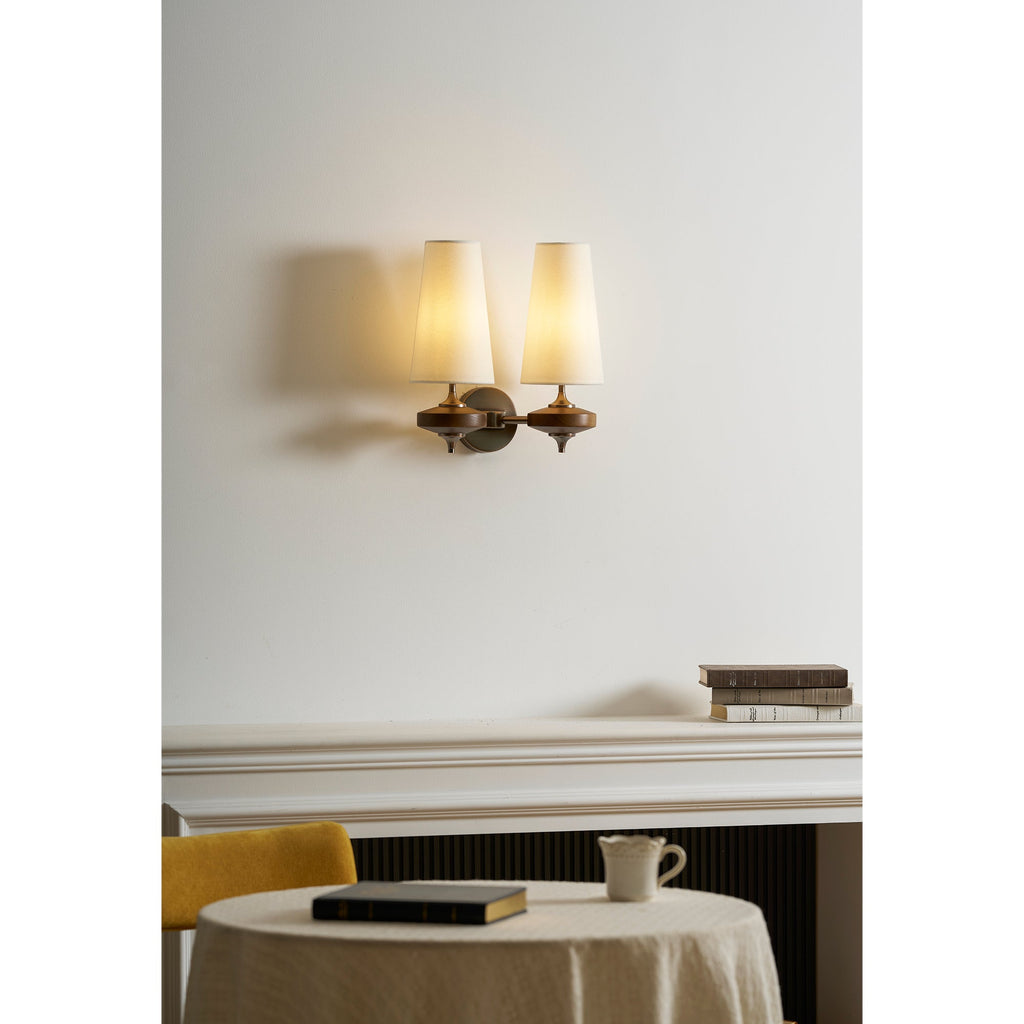Warm glow from two cream shades on a Clérachic twin sconce, above a mantel, a mustard chair and a laid table.