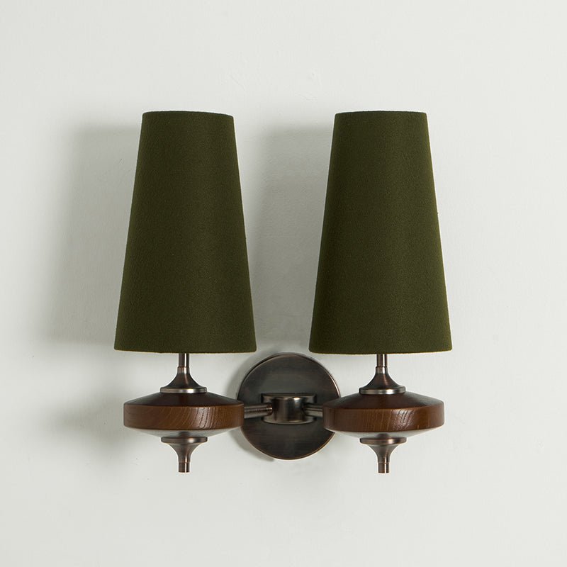 Unlit green shades on a Clérachic twin sconce with walnut discs and a chain-link bronze arm, on a pale wall.