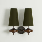 Unlit green shades on a Clérachic twin sconce with walnut discs and a chain-link bronze arm, on a pale wall.