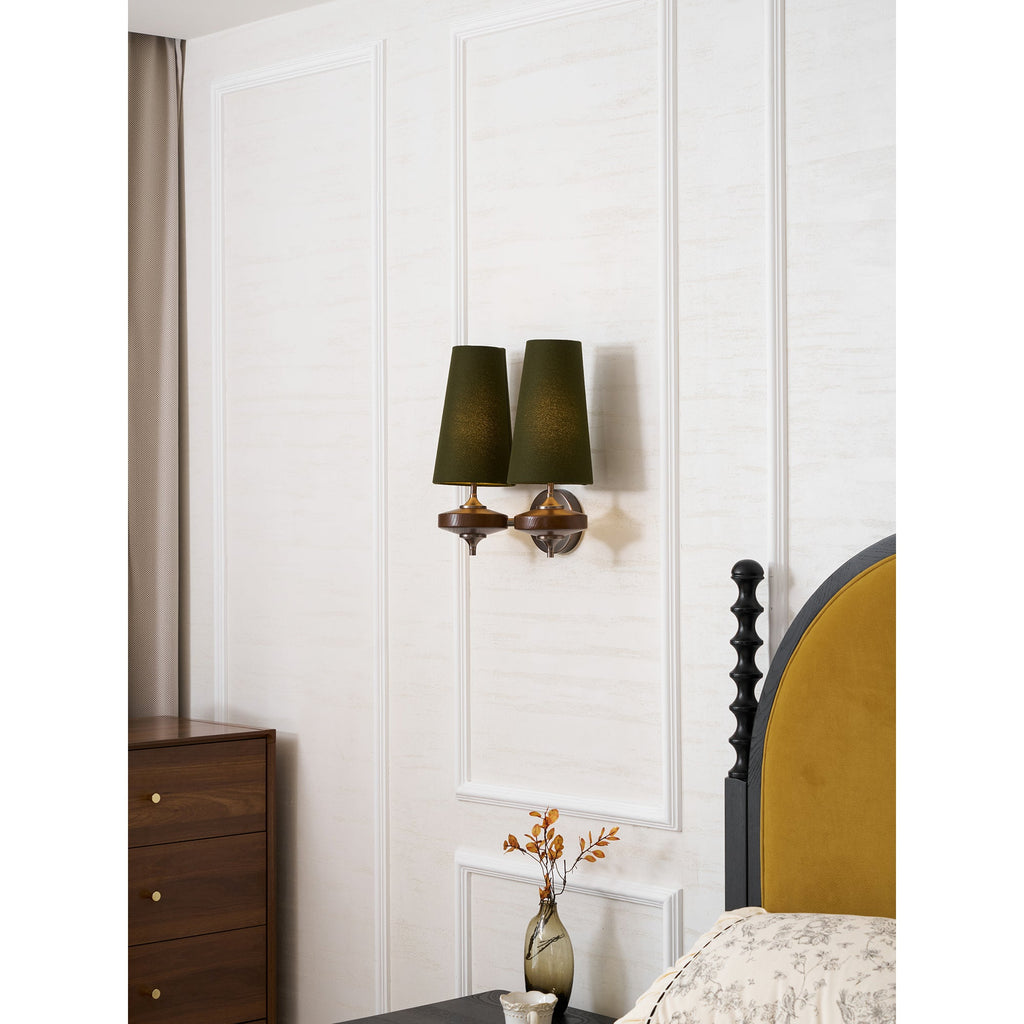A Clérachic twin sconce with green shades above a walnut chest of drawers and a bed with a mustard headboard.