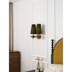 A Clérachic twin sconce with green shades above a walnut chest of drawers and a bed with a mustard headboard.