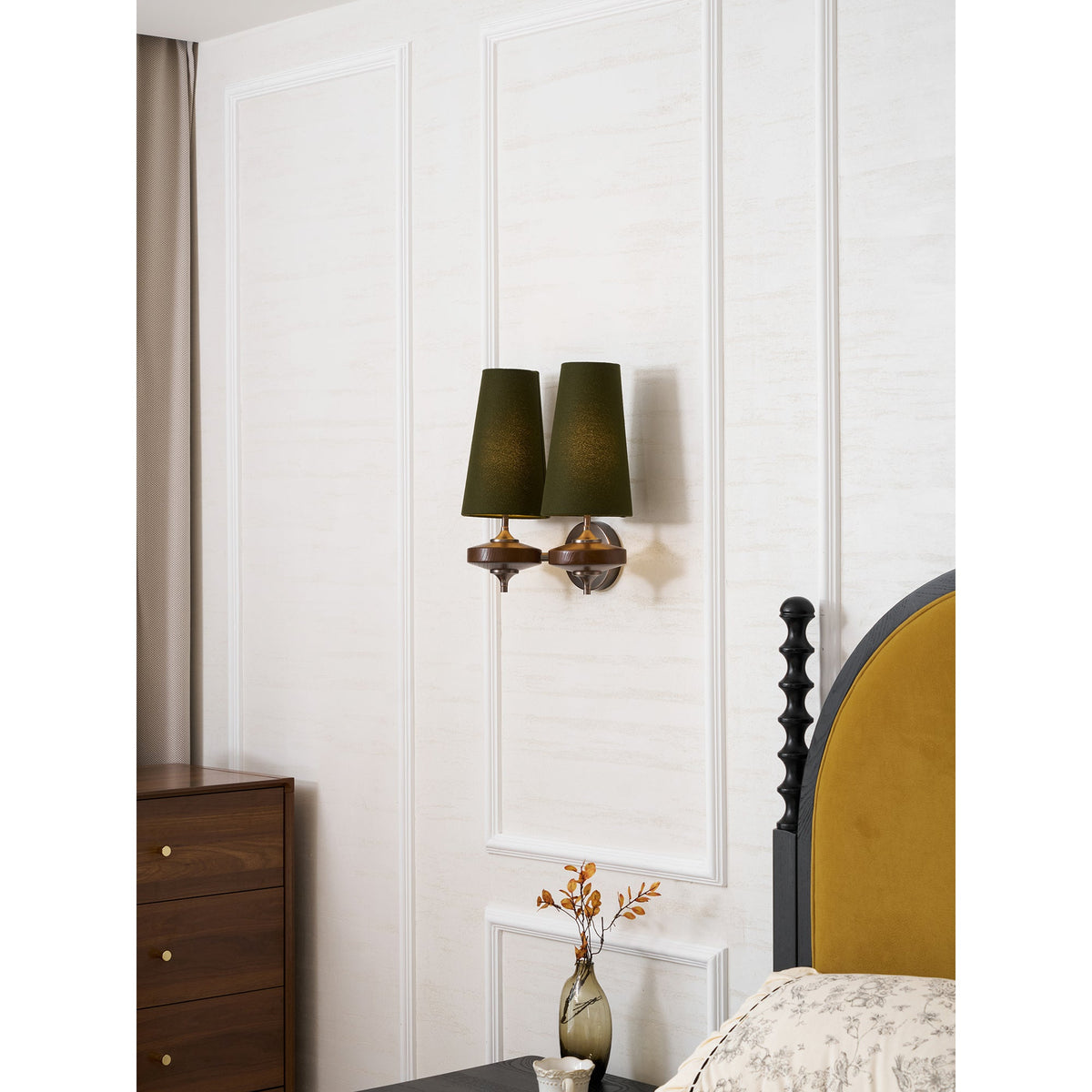A Clérachic twin sconce with green shades above a walnut chest of drawers and a bed with a mustard headboard.