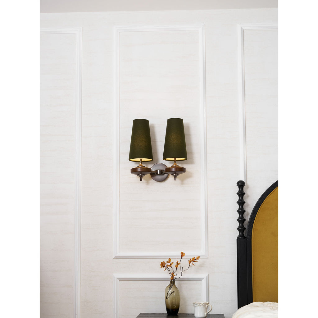 A small Clérachic twin sconce with lit green shades, centred on a white panelled wall above a vase of autumn stems.