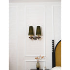A small Clérachic twin sconce with lit green shades, centred on a white panelled wall above a vase of autumn stems.