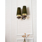 Close, angled view of a lit Clérachic twin sconce in green, with one arm turned out, on a white panelled wall.
