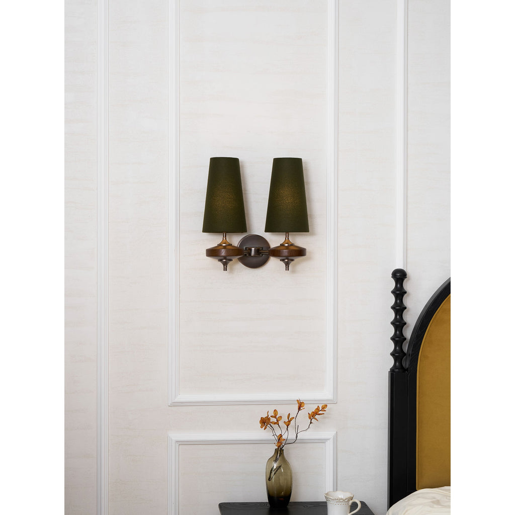 Unlit green shades on a Clérachic twin wall light, hung on a white panelled wall over a bedside vase and mug.