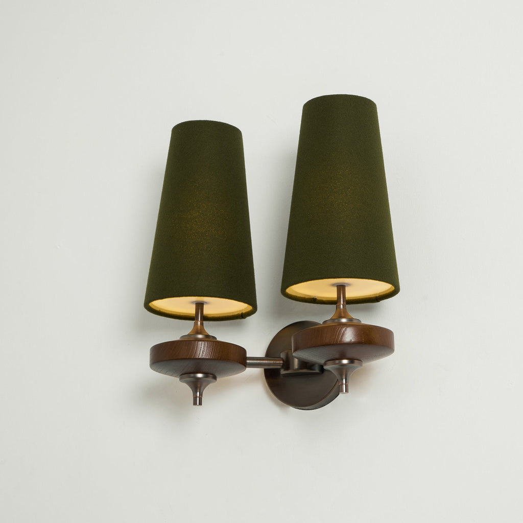Angled view of a Clérachic twin wall sconce with lit green shades, gold glowing inside, on a pale mint wall.