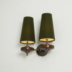 Angled view of a Clérachic twin wall sconce with lit green shades, gold glowing inside, on a pale mint wall.