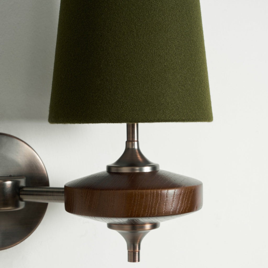 Close view of a green fabric shade, bronze stem and walnut disc on this Clérachic wall sconce, against white.
