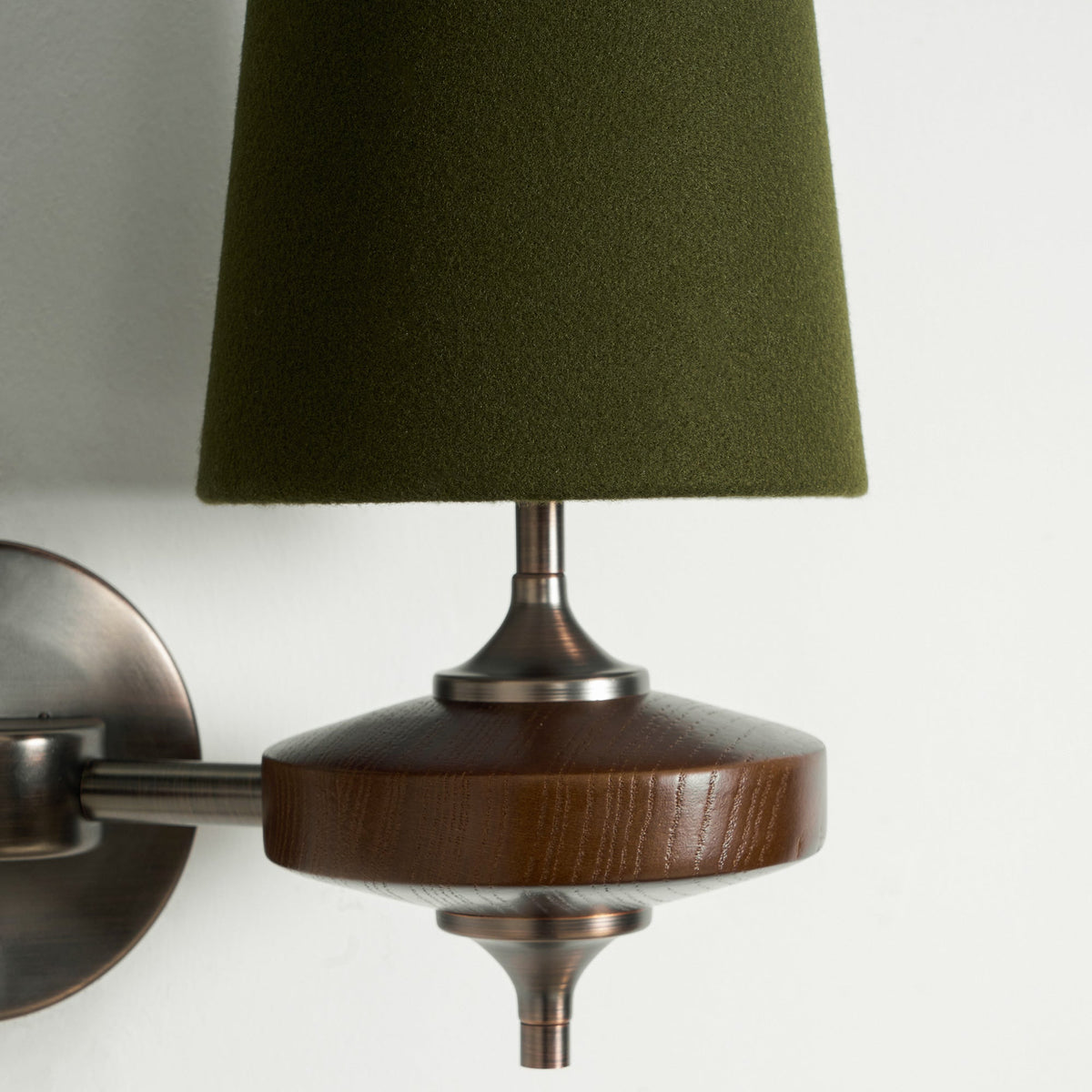 Close view of a green fabric shade, bronze stem and walnut disc on this Clérachic wall sconce, against white.