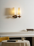 Warmly lit cream shades on a Clérachic twin sconce, above a white mantel with books and a laid round table.