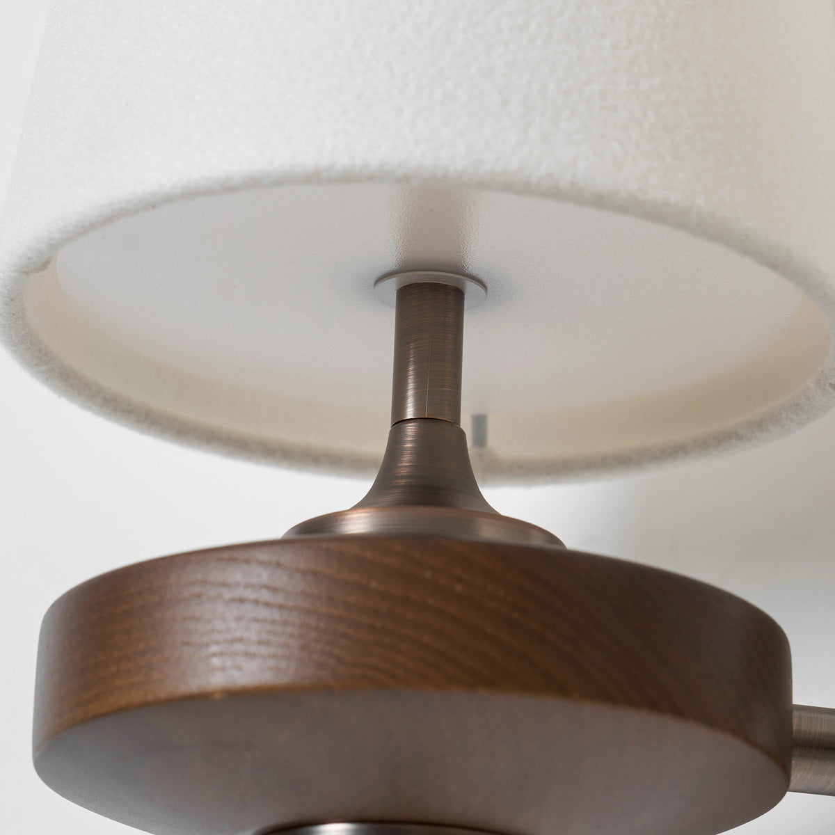 Close view of the underside of a cream shade with its bronze stem and a grained walnut disc, on this Clérachic sconce.