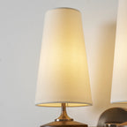 Close view of a lit cream shade and part of its twin on a Clérachic wall sconce, with a bronze stem and backplate.