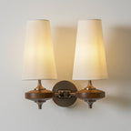Two lit cream shades fill the frame on this Clérachic twin sconce, with walnut discs and a round bronze backplate.