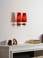 Angled view of a Clérachic twin sconce with red shades, over a white mantel with books and a small gilt mirror.