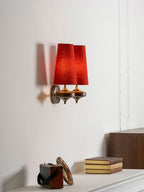 A Clérachic wall sconce with two red shades seen at an angle, above a mantel with a stack of books and an old case.