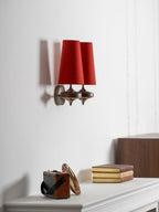 Side view of a Clérachic red twin sconce on a white wall, above a mantel shelf with books and a small leather-trimmed box.