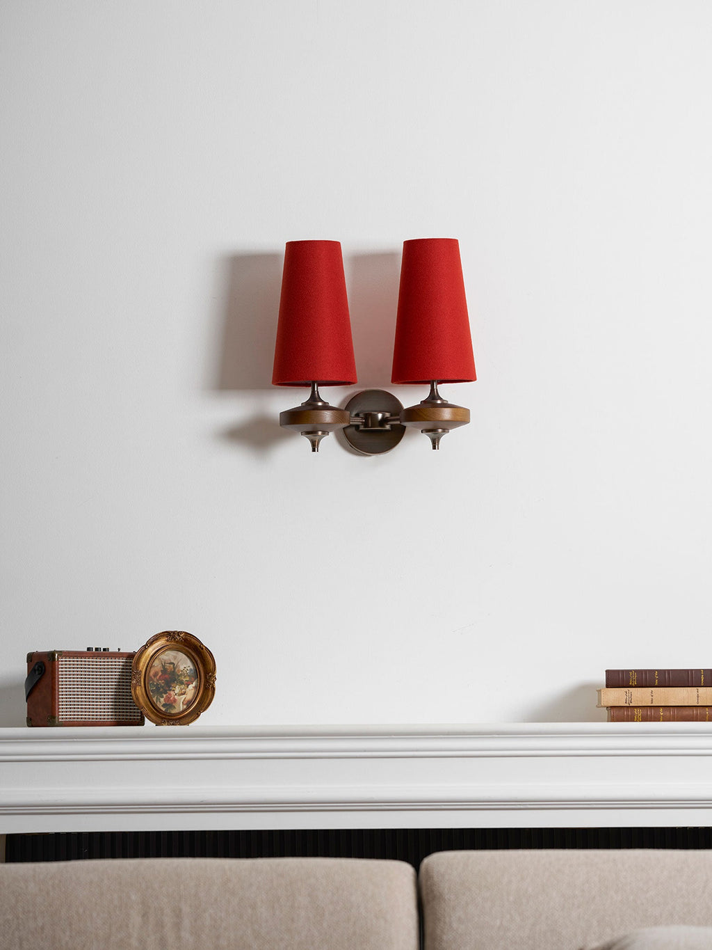 A small Clérachic twin sconce with red shades above a white mantel, a vintage radio and a taupe sofa.