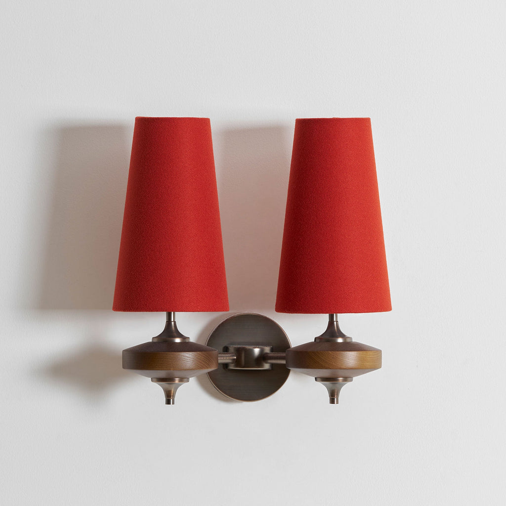 Two red fabric shades fill this close view of a Clérachic twin wall sconce, with walnut discs and a bronze plate below.