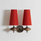 Two red fabric shades fill this close view of a Clérachic twin wall sconce, with walnut discs and a bronze plate below.