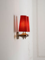 Side-on view of a Clérachic wall sconce with two red shades beside a white panelled door frame.