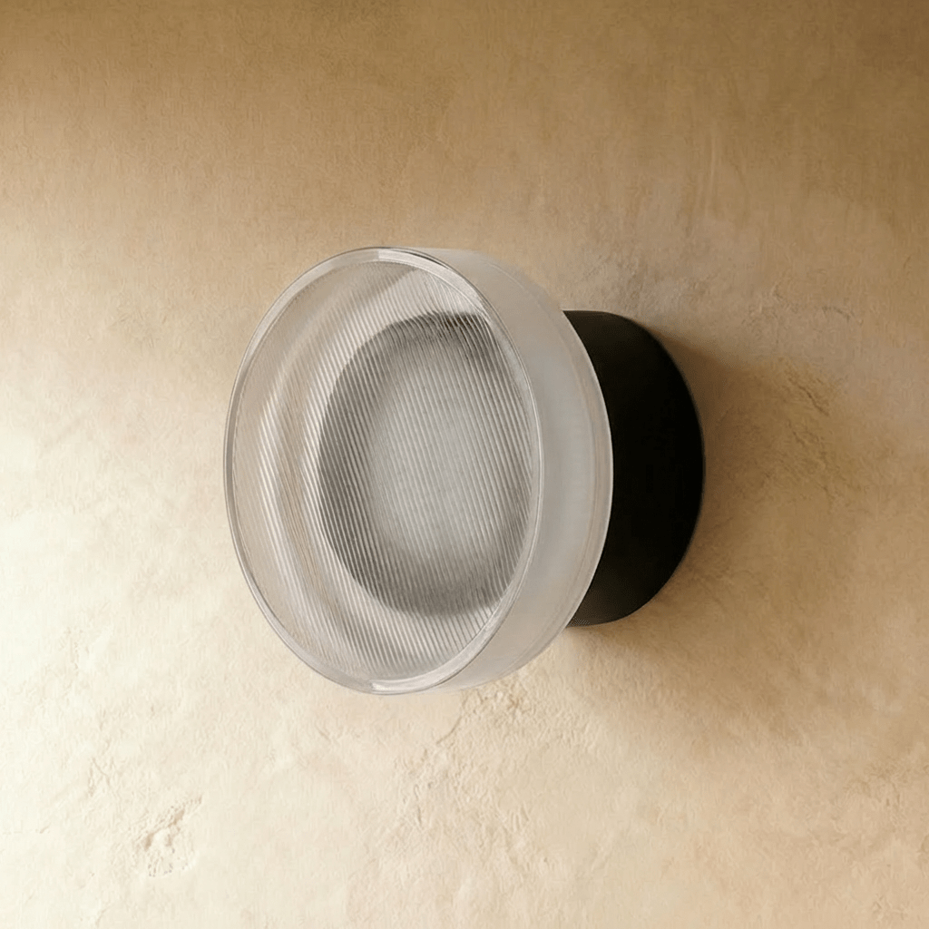 Clérachic round wall light switched off, showing its finely ribbed glass shade on a matt black wall plate and limewash plaster.
