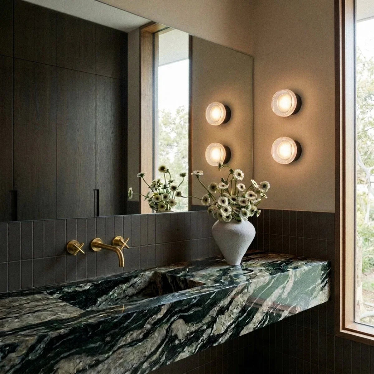 Two pairs of Clérachic round ribbed-glass wall lights glowing warm beside a mirror above a green marble basin with brass taps.