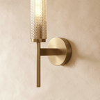 Clérachic brushed brass wall sconce close up, showing the faceted glass cylinder, slim stem and round wall plate.
