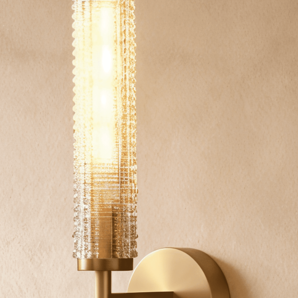 Clérachic brass wall sconce close up with a glowing beaded glass cylinder above a brass collar and round wall plate.