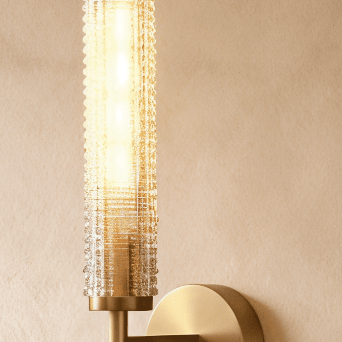 Clérachic brass wall sconce close up with a glowing beaded glass cylinder above a brass collar and round wall plate.