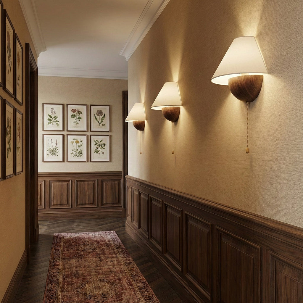 A row of three Clérachic wall lights glowing along a panelled hallway, with framed botanical prints at the far end.