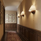 A row of three Clérachic wall lights glowing along a panelled hallway, with framed botanical prints at the far end.