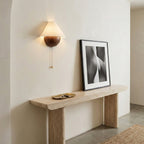 Clérachic wall light on a cream wall above a pale stone console table, with a framed black-and-white print leaning below.