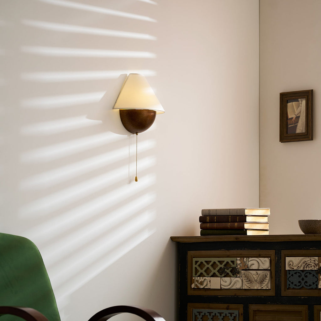 Clérachic wall light seen from further back, with sun stripes on the wall and a patterned wooden cabinet beneath it.