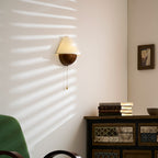 Clérachic wall light seen from further back, with sun stripes on the wall and a patterned wooden cabinet beneath it.