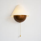 Lit Clérachic wall light in an aged bronze finish on a white wall, with a long beaded pull chain hanging down.