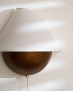 Close view of the fabric shade and textured bronze half-sphere on this Clérachic wall light, with sun stripes across it.