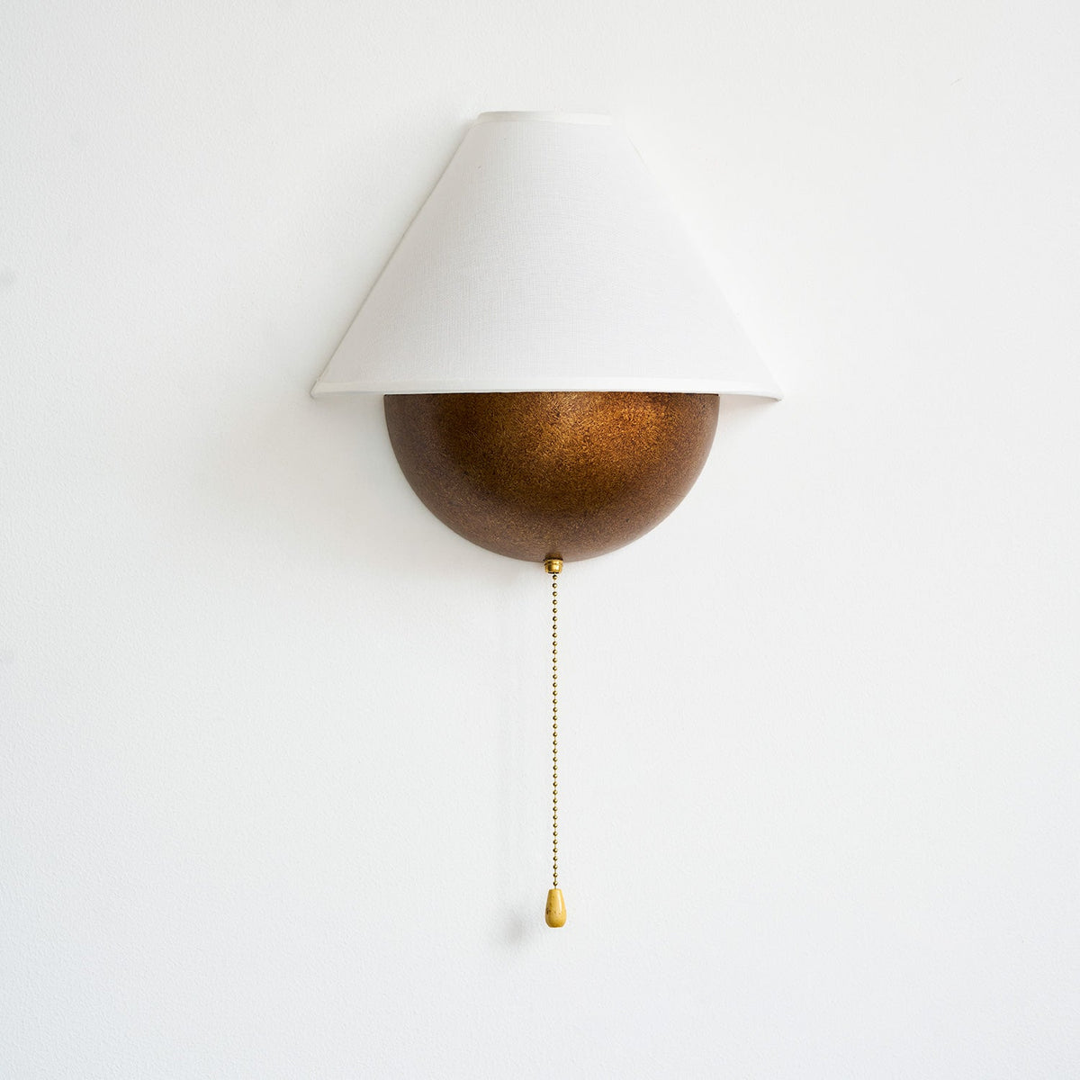 Unlit Clérachic wall light with a white fabric shade and a speckled bronze half-sphere, on a plain white wall.