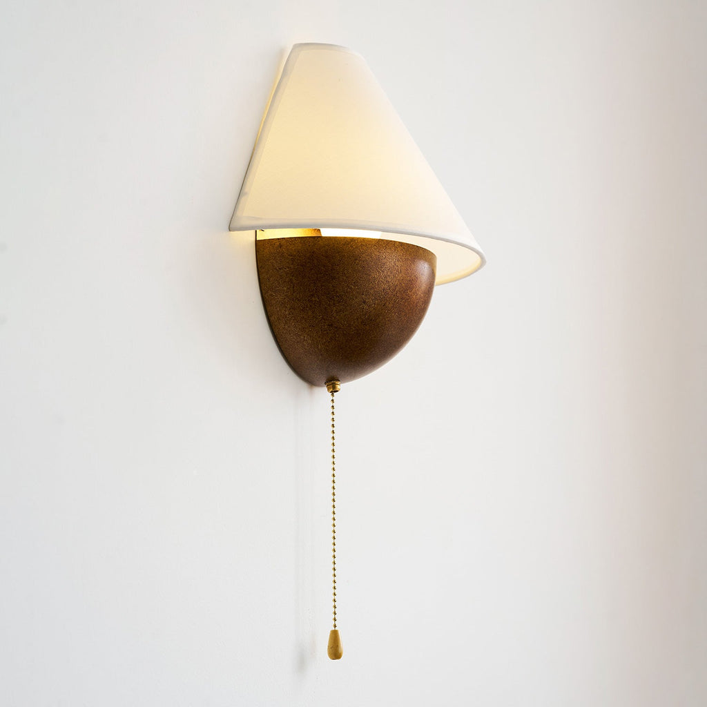 Clérachic wall light with the glow showing inside the shade, angled to show the curved base and its beaded chain.