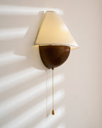 Clérachic wall light lit in sun stripes, with the shade tilted forward and a long chain hanging from the base.